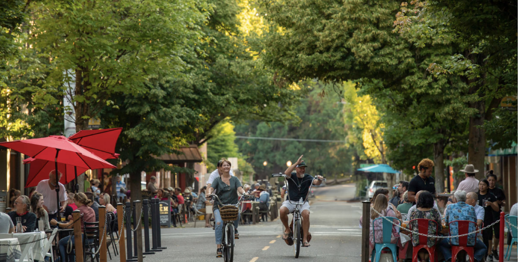 Photo of 3rd street during Mac Fresco in downtown McMinnville with two people on bikes and multiple tables of diners on the street